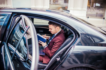 Smiling businessman checking his notebook inside a car