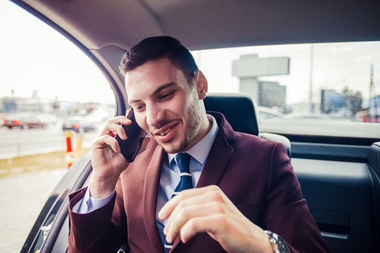 Happy young businessman sitting in limousine, talking on mobile