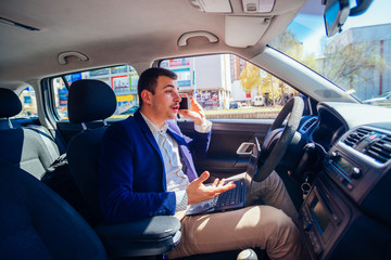 Reckless businessman driving in the city during the rush hour while typing on his laptop and acting stressed out of work.