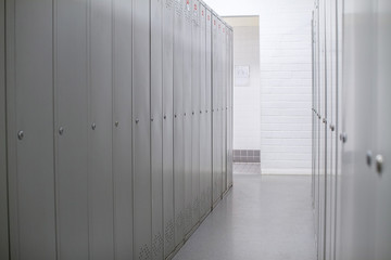 A row of steel grey lockers along the white wall. Dressing room at the enterprise or in the gym. Narrow corridor