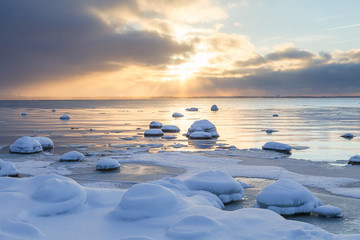 Sunset with snowy boulders and beach landscape. Baltic sea, winter time.