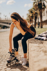 Happy joyful young woman wearing roller skates sitting in town