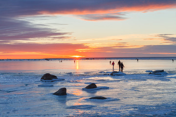 People walking on the frozen sea surface at sunset, Estonia.