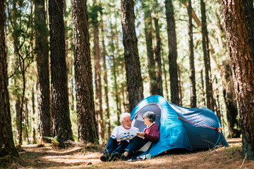 Active people old aged caucasian senior couple travel with camping tent - sit down in the forest...