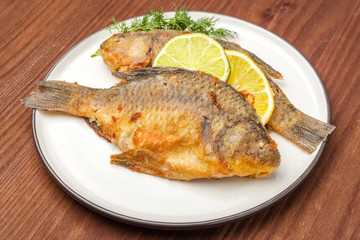Fried fish with slices of lemon and lime on a plate. Close up ready dish
