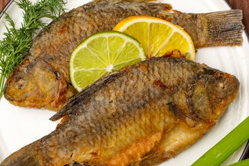 Grilled Crucian fish decorated with lemon slices with lime and fresh herbs. finished dish closeup