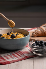 Sweet breakfast with corn flakes, croissant with berry and honey. Healthy food on table