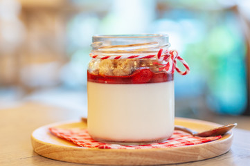 Strawberry Panna Cotta in glass can lay on circle wooden tray with stainless spoon and red cross napkin.