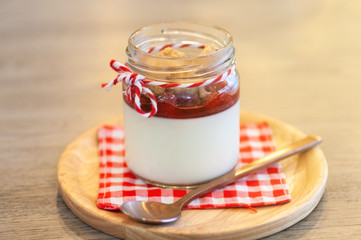 Strawberry Panna Cotta in glass can lay on circle wooden tray with stainless spoon and red cross napkin.