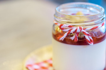 Strawberry Panna Cotta in glass can lay on circle wooden tray with stainless spoon and red cross napkin.