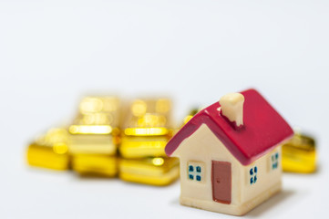 Selective focus miniature home red roof with stack of golden bars, saving and invest for new residence.  Real estate business investment with gold.