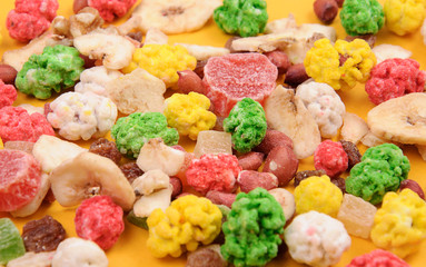 Mix nuts, dried and candied fruits . Cleaned kernels of peanut, walnut, assortment of peanut in colored sugar, candied fruits, raisin and banana chips on yellow background. Selective focus.