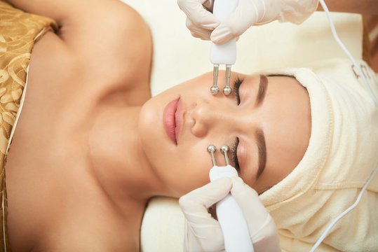 Portrait of beautiful young woman getting laser procedure for her face with the help of cosmetologist in spa salon