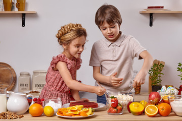 Little friends are making a cake together at a kitchen against a white wall with shelves on it.