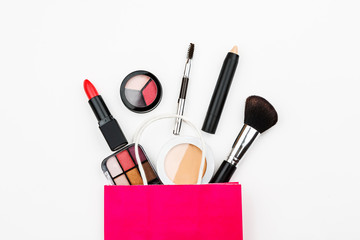 Set of makeup cosmetic: shadows, brushes, lipstick on a white background with colored shopping bags, top view