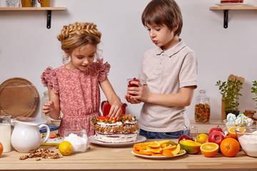Little friends are making a cake together at a kitchen against a white wall with shelves on it.