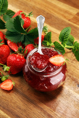 strawberry jam with fresh strawberries and mint. marmalade on spoon and jar on brown wood