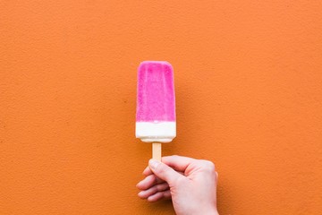 Tasty and cold ice cream of pink and white shades against the background of orange color. Ice cream expensive in the hands of a gentle female hand.