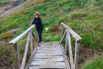 Naklejka premium Mature redhead woman, with sportswear, leaning against a wooden bridge, with meadows in the background, a cloudy spring afternoon