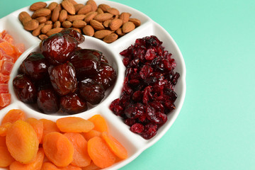 Mix of dried fruits and nuts on a white plate. Apricot, almond, raisin, dates fruit. On a brown background. Space for text or design.