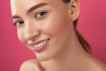 Joyful girl with perfect skin standing against pink background