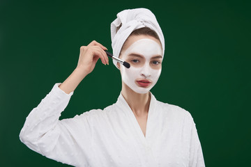 Beautiful young woman applying facial mask with brush