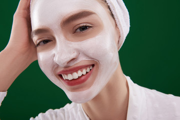 Cheerful lady with cosmetic mask on her face touching towel on head