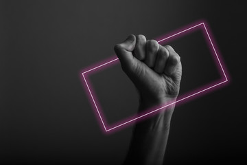 Raised clenched fist against a dark background with abstract neon light glow