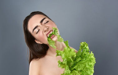 Woman is actively eating salad against grey background