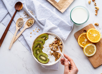 Female hand hold spoon over healthy breakfast bowl enjoy detox morning meal on table background, woman vegan eat natural fruit nut granola nutrition with yoghurt, detox organic food concept, top view