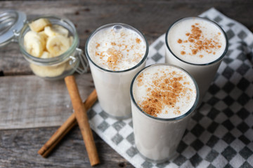 Banana smothie or milkshake with cinnamon on wood background