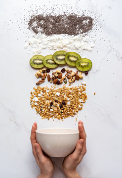 Healthy breakfast concept, female hand holding bowl with granola nuts kiwi chia seeds on white background, morning organic food with diet on table, detox meal for health nutrition vertical top view