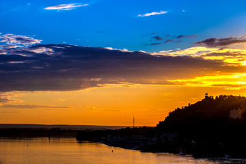 Silhouette of monument to Salawat Yulaev against a bright yellow blue sky with clouds and orange sun disk at city sunset on the river bank. Salavat Yulayev, Ufa, Bashkortostan, Russia.