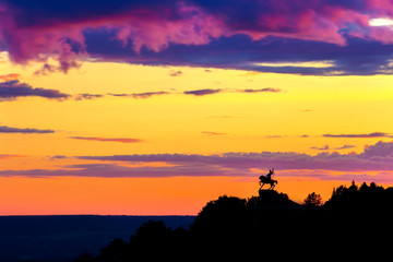 Silhouette of monument to Salawat Yulaev, folk hero on a horse against a bright yellow purple violet sky with clouds and orange sun disk at city sunset. Salavat Yulayev, Ufa, Bashkortostan, Russia.