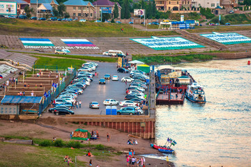 Pier on the beach in the city center, car parking, volleyball court and resting people, flags of Russia and Bashkortostan on the embankment. White river, Ufa, Bashkortostan, Russia - June 2015.