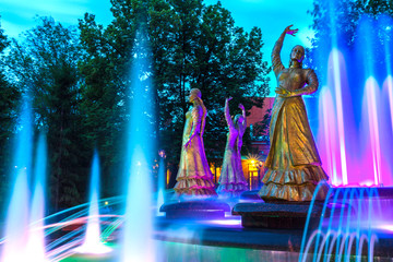 Sculptures of beautiful girls in national dresses in a multi-colored highlight against the background of the night evening sky. Seven Girls Fountain, Ufa, Bashkortostan, Russia - June 2015.