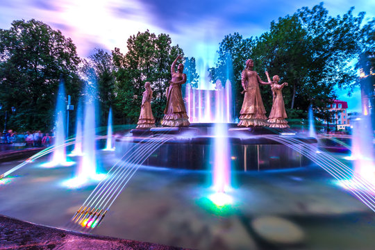 Sculptures of beautiful girls in national dresses in a multi-colored highlight against the background of the night evening sky. Seven Girls Fountain, Ufa, Bashkortostan, Russia - June 2015.