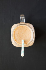 Healthy banana apple smoothie in a glass jar over black background, view from above. Flat lay, top view, overhead.