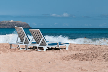 Two empty deck chairs on a deserted sandy beach on the ocean.