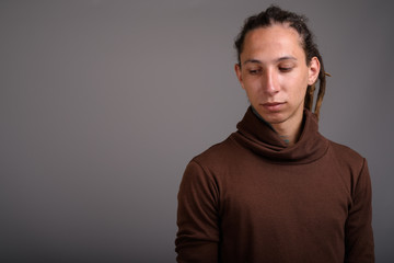 Young man with dreadlocks wearing brown shirt against gray backg