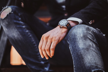Closeup photo shoot of watch on the man's hand.He is wearing ripped jeans.