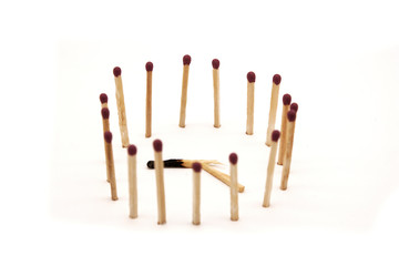 matches stand in the circle around a broken burnt match on a white background