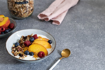 Granola with yogurt fresh peach, blueberry, raspberry on the table - healthy breakfast