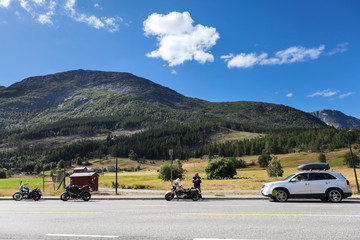 Fototapeta premium Three motorcycles and car standing on roadside of highway in mountains of Norway. Travel in Scandinavia by vehicles
