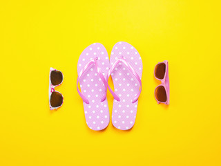 Summer flat lay. Beach accessories pink flip flops and sunglasses on yellow background. Summer...