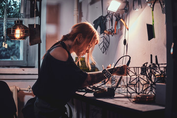 Talanted young woman is working on her own project at glass workshop. - obrazy, fototapety, plakaty