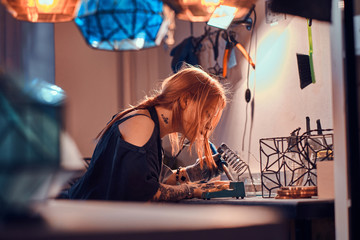 Dilegent pensive woman is working on her own lamp project at cozy workshop.
