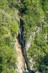 Fototapeta na wymiar The view from the height of the high waterfall falling into a lake in a green forest