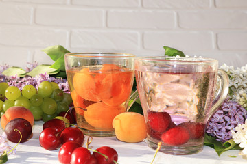 Apricot and cherry juice, apricots, cherries and grapes on a sunny table. Summer drinks and fruits during a break with colorful branches of lilac, selective focus