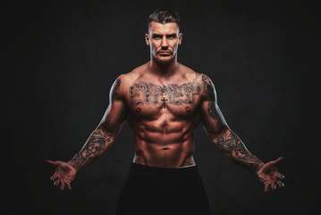 Fototapeta na wymiar A tattooed muscular shirtless man with stylish hair posing at the camera on a dark background.